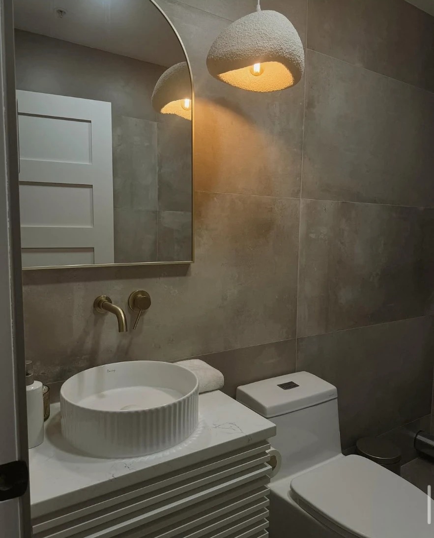 Powder bath with concrete-look large-format tile, fluted vessel sink and gold wall-mount faucet