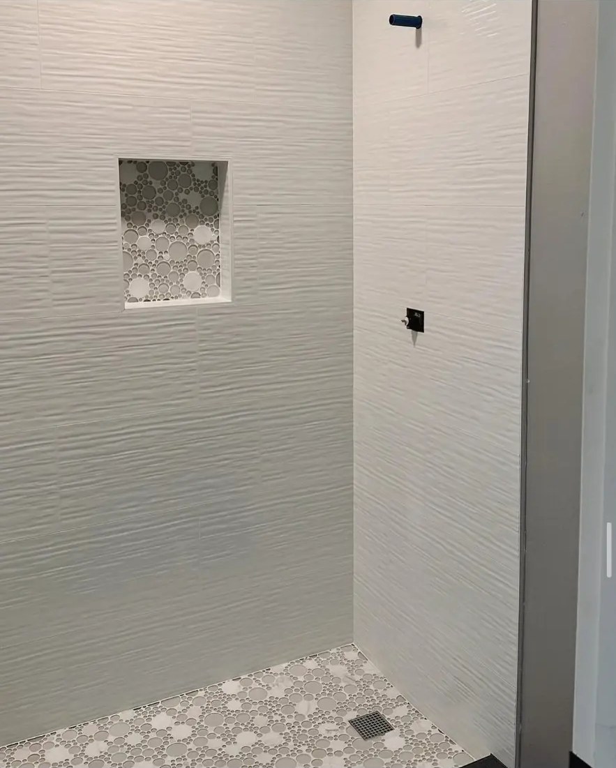 White textured tile shower with mosaic niche and circular pebble floor tile