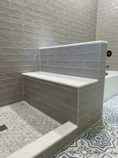 Tiled shower bench with gray subway tile walls and hexagon mosaic floor