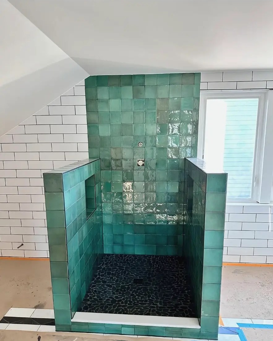 Green square ceramic tile shower with black pebble floor and subway tile walls