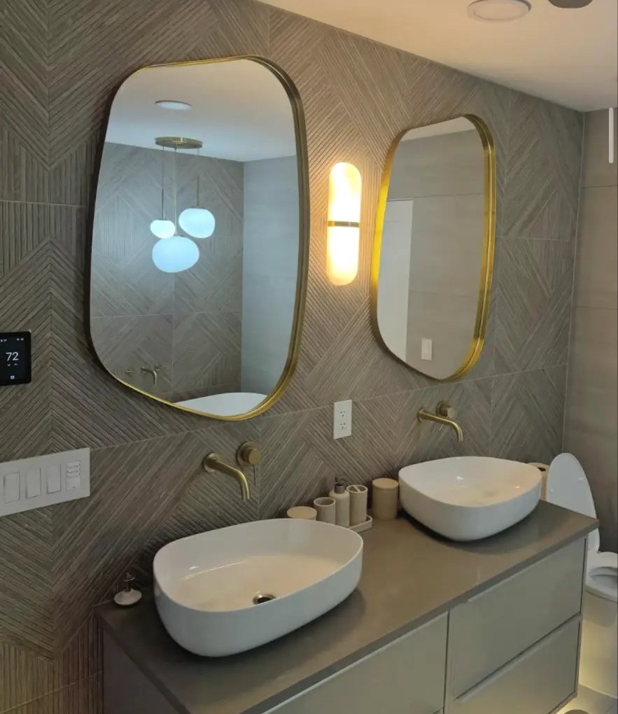 Double vessel sink vanity with gold fixtures and patterned tile wall