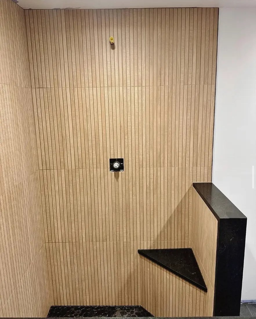 Wood-look vertical tile shower with black stone bench and pebble floor