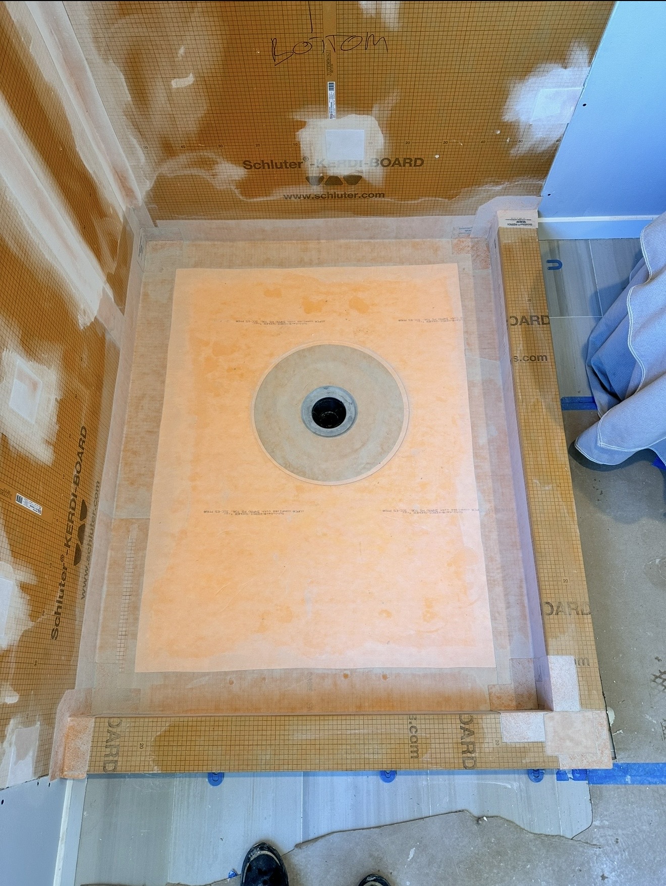 Sloped shower pan waterproofing tied into the drain assembly and continuing up the walls