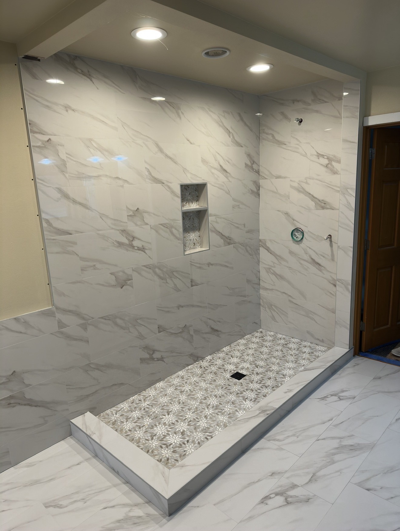 Marble-look tiled walk-in shower with decorative mosaic floor and built-in niche