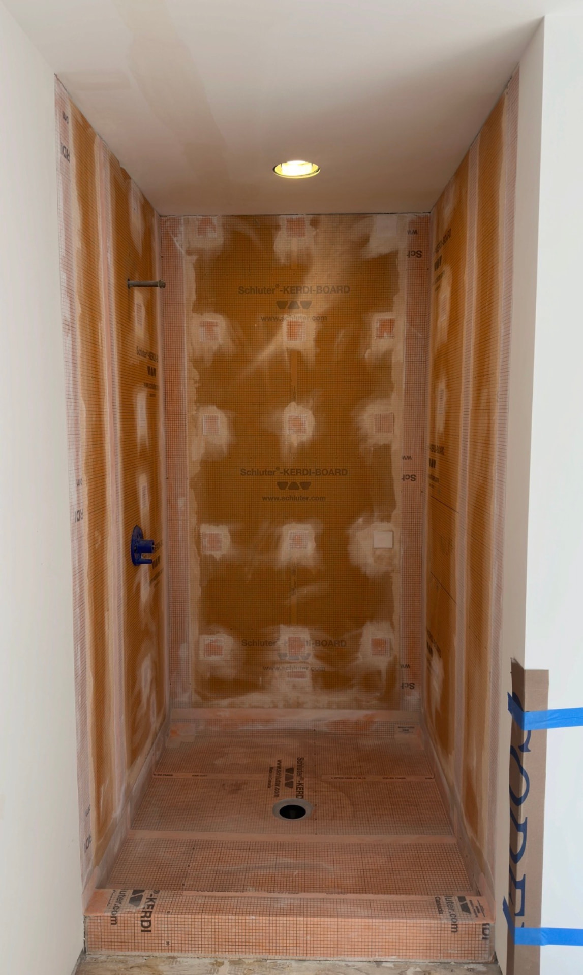 Walk-in shower with waterproof board walls and a seam-sealed sloped shower pan before tile