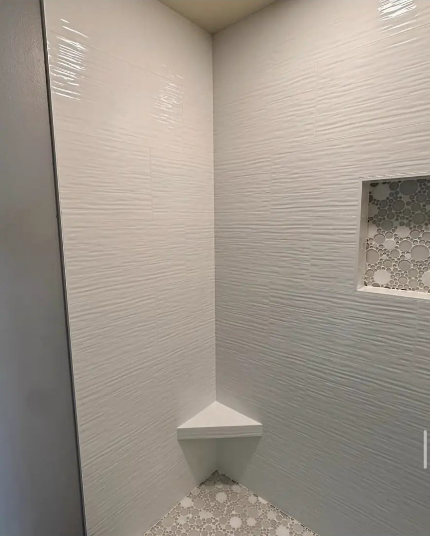 All-white textured tile shower with corner bench and mosaic niche