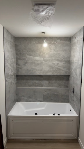 Soaking tub alcove with light gray large-format tile surround and inset shelf ledge