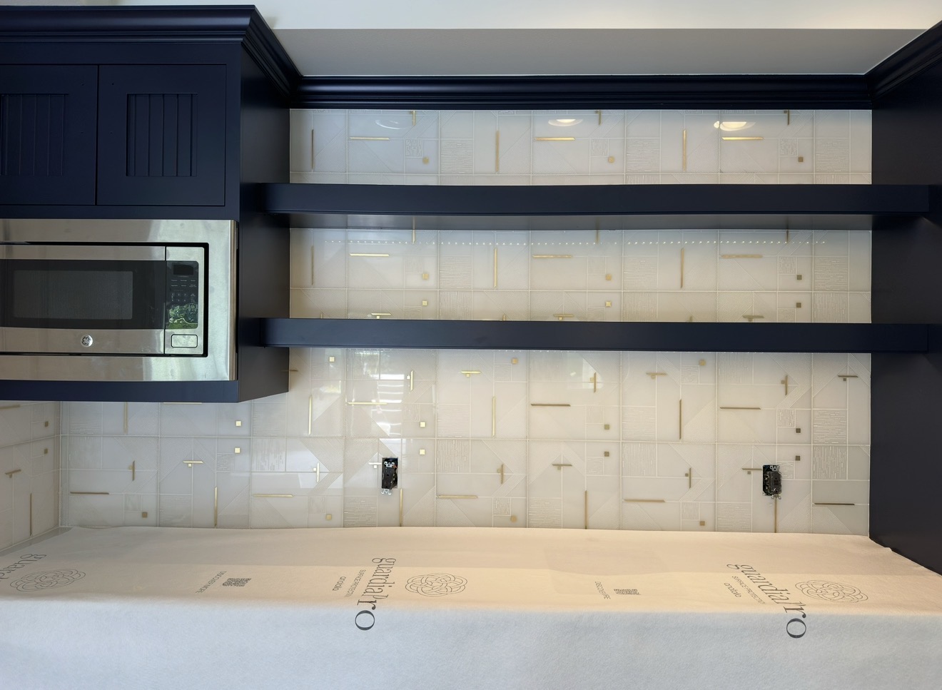 White textured tile kitchen backsplash with gold inlay accents behind navy cabinetry