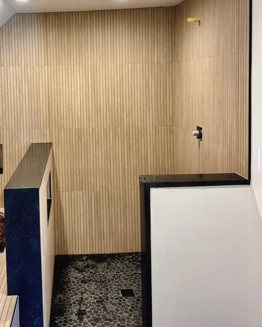 Vertical wood-look tile walls with black pebble tile shower floor